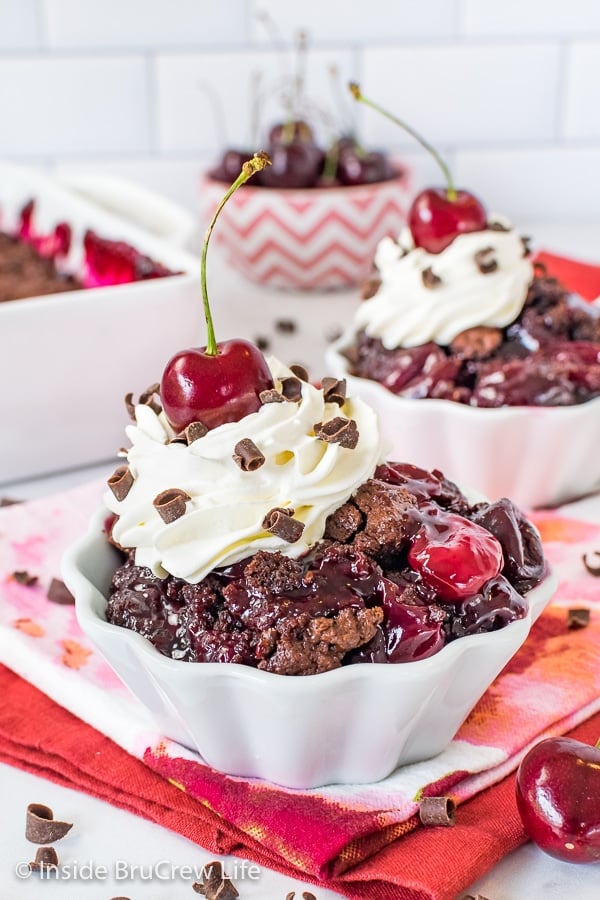 A white bowl filled with chocolate cherry cobbler with a pan of cobbler behind it