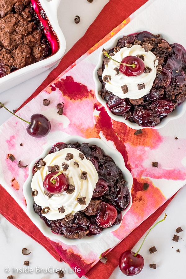 Overhead picture of two white bowls filled with chocolate cherry cobbler topped with whipped cream and a cherry