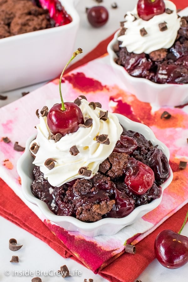 A white bowl filled with chocolate cherry cobbler topped with homemade whipped cream and a cherry