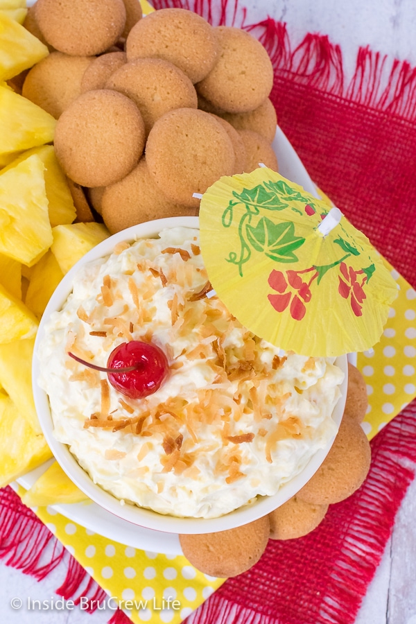 Overhead picture of a bowl of pina colada fruit dip on a plate with vanilla wafers and pineapple wedges