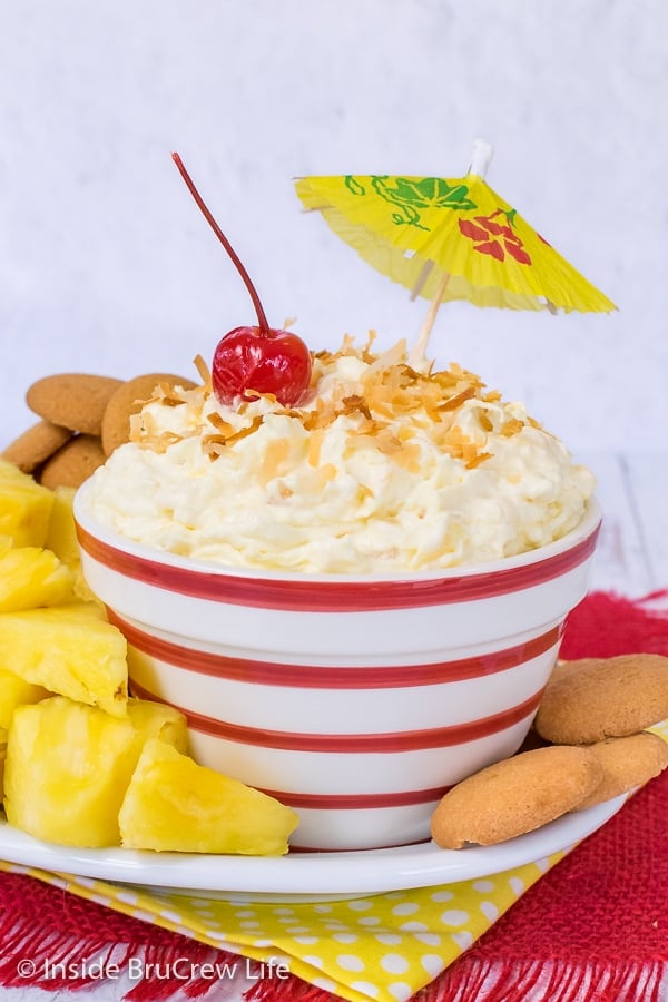 A red and white striped bowl filled with pina colada fruit dip and pineapple wedges and vanilla wafers around it