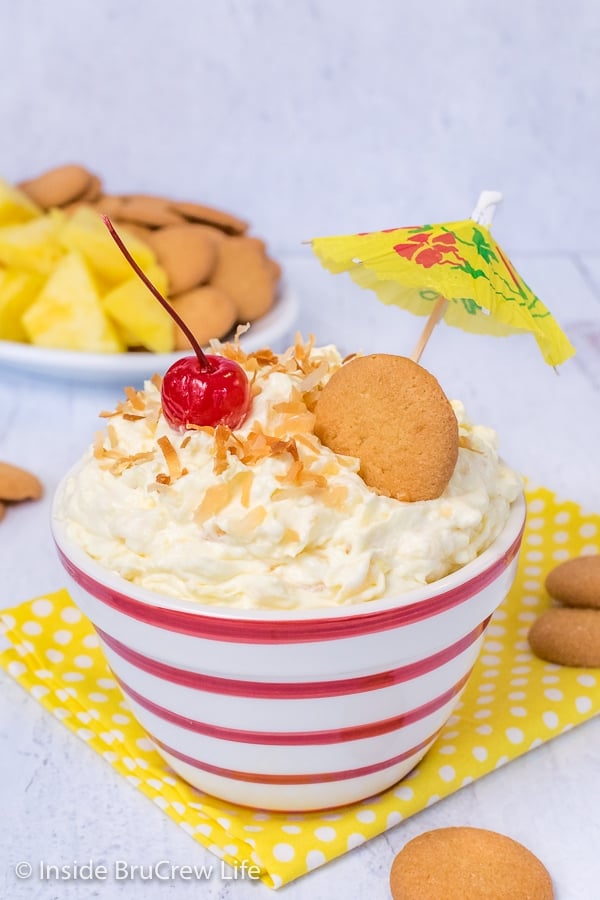 Red and white striped bowl filled with pina colada fruit dip and topped with coconut and a cherry