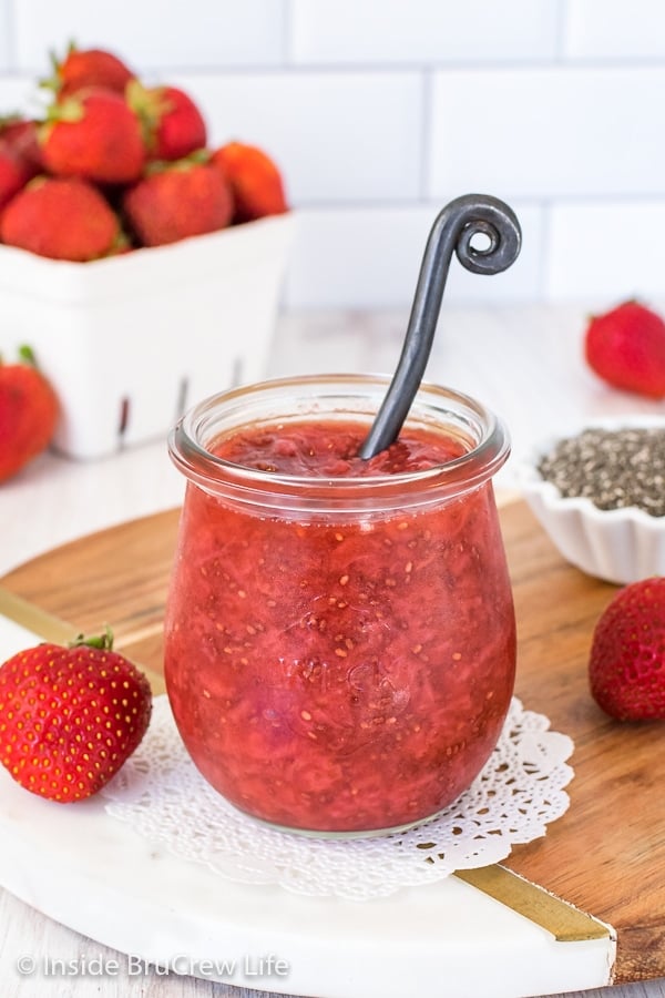 A clear jar filled with strawberry chia jam and strawberries behind it