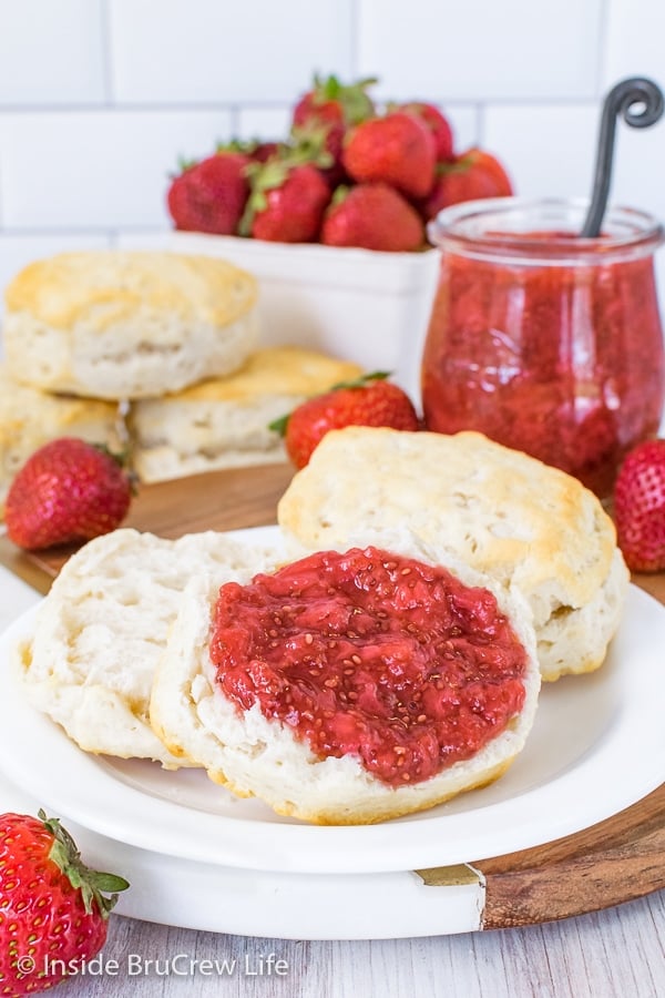 An open biscuit on a white plate with strawberry chia jam on it and a jar of jam behind it