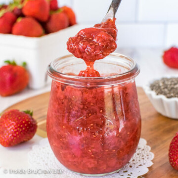 A clear jar filled with strawberry chia jam and a spoon lifting jam out