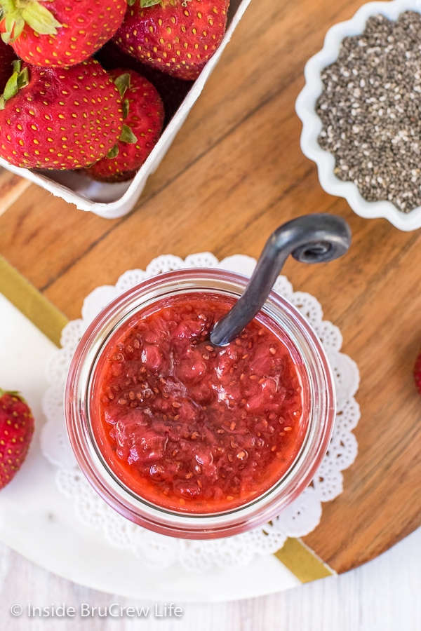 Overhead picture of a jar of strawberry chia jam, a container of strawberries, and bowl of chia seeds