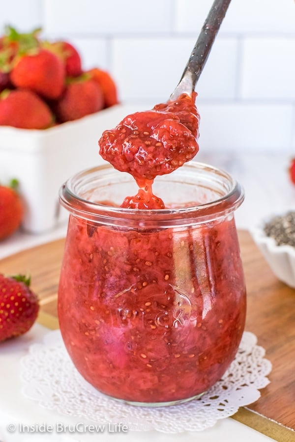 A clear jar filled with strawberry chia jam and a spoon lifting out a spoonful of the jam