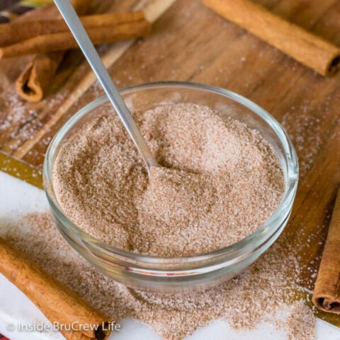 A clear bowl on a wooden board filled with homemade cinnamon sugar and a spoon.