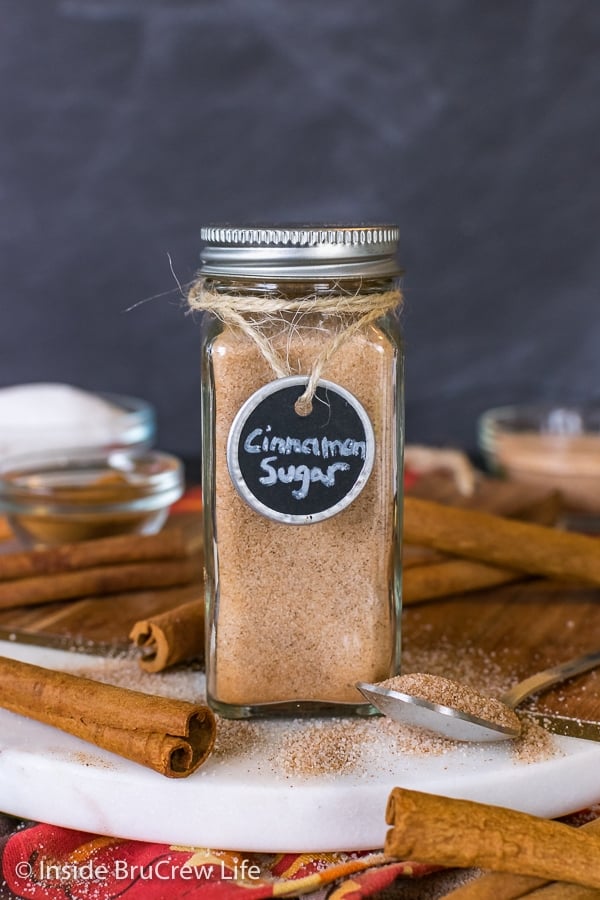 A clear spice jar filled with homemade cinnamon sugar on a tray with cinnamon sticks.