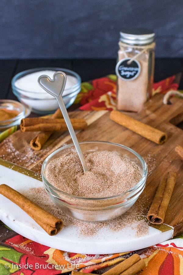 A clear bowl filled with a cinnamon sugar and a spoon on a wood tray.