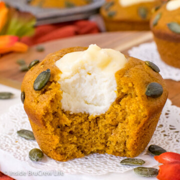 A pumpkin cream cheese muffin on a white doily with a bite taken out of it showing the filling center