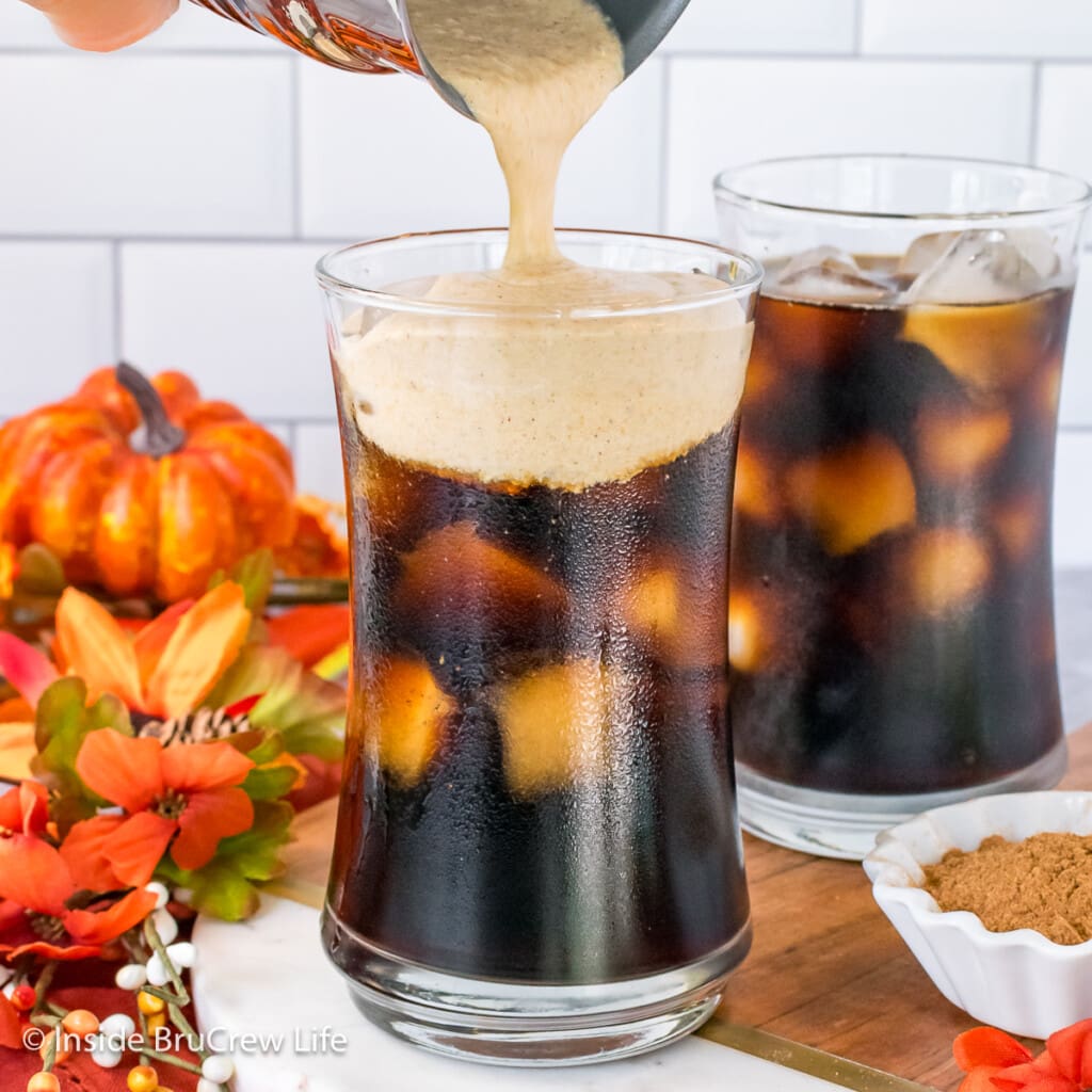 Two cups of iced coffee with cold foam being poured on top.