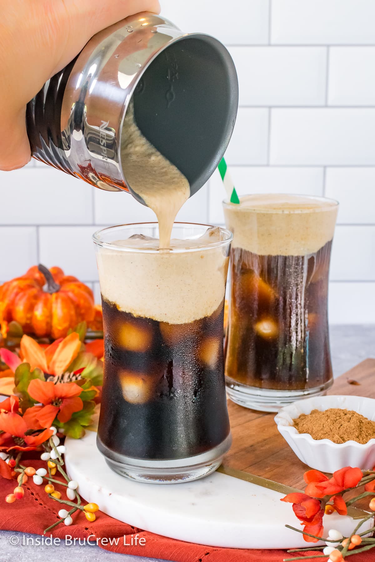 Two clear glasses with iced coffee and cold foam.