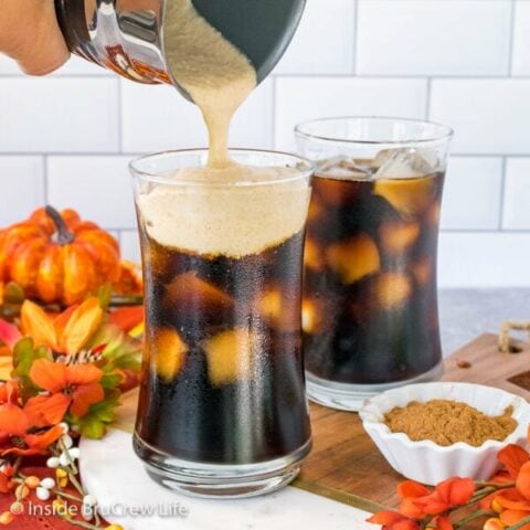 Two glasses of iced pumpkin cream cold brew on a tray with pumpkin cold foam being poured into the front glass