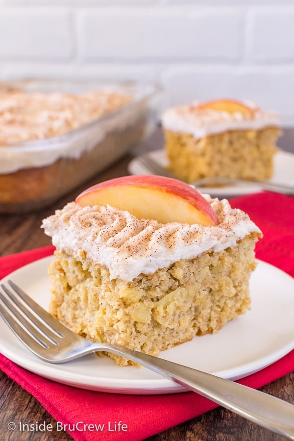 A square of snickerdoodle apple cake on a white plate topped with cinnamon frosting and apple slices.