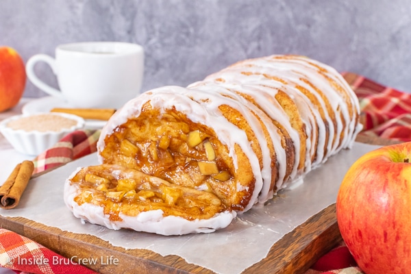A loaf of apple cinnamon pull apart bread drizzled with glaze on a wood tray