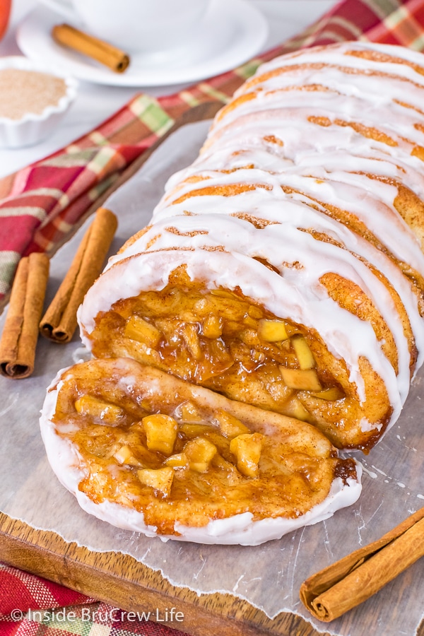 A slice of apple cinnamon pull apart bread lying on a wood board with the rest of the loaf behind it