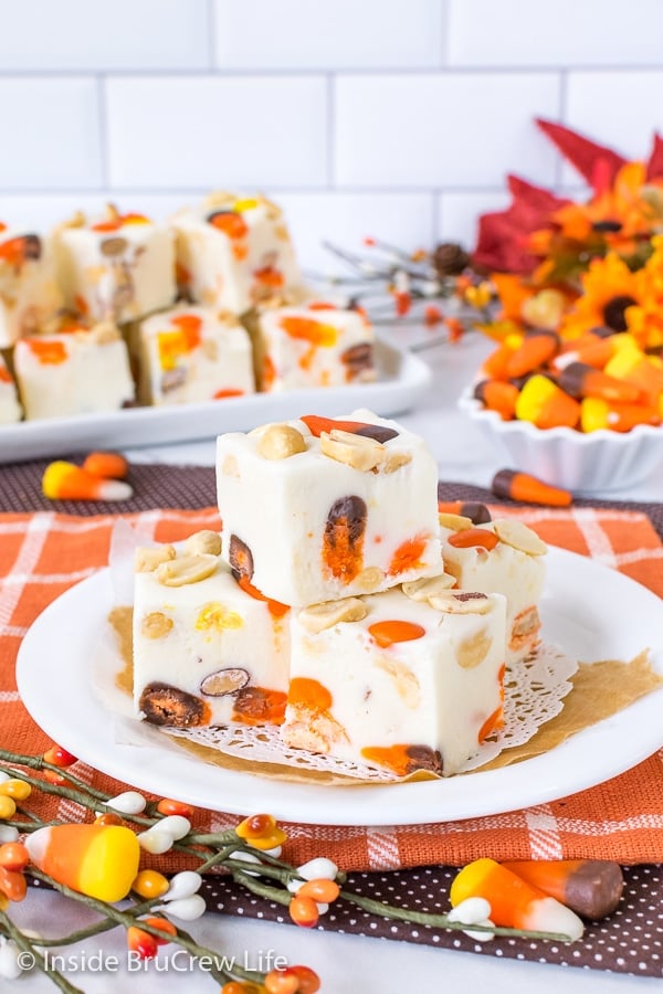 An orange towel with a white plate on it with squares of candy corn fudge stacked on it