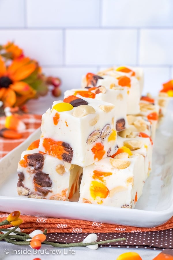 A white plate on an orange towel with white chocolate candy corn fudge stacked on it