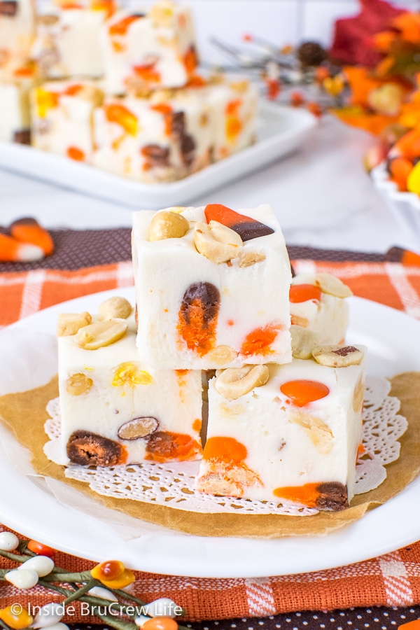 A white plate on an orange towel with squares of candy corn fudge on it and more behind it