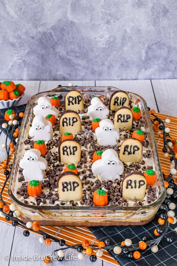 A pan of Chocolate Pumpkin Lasagna decorated with tombstone cookies, marshmallow ghosts, and candy pumpkins