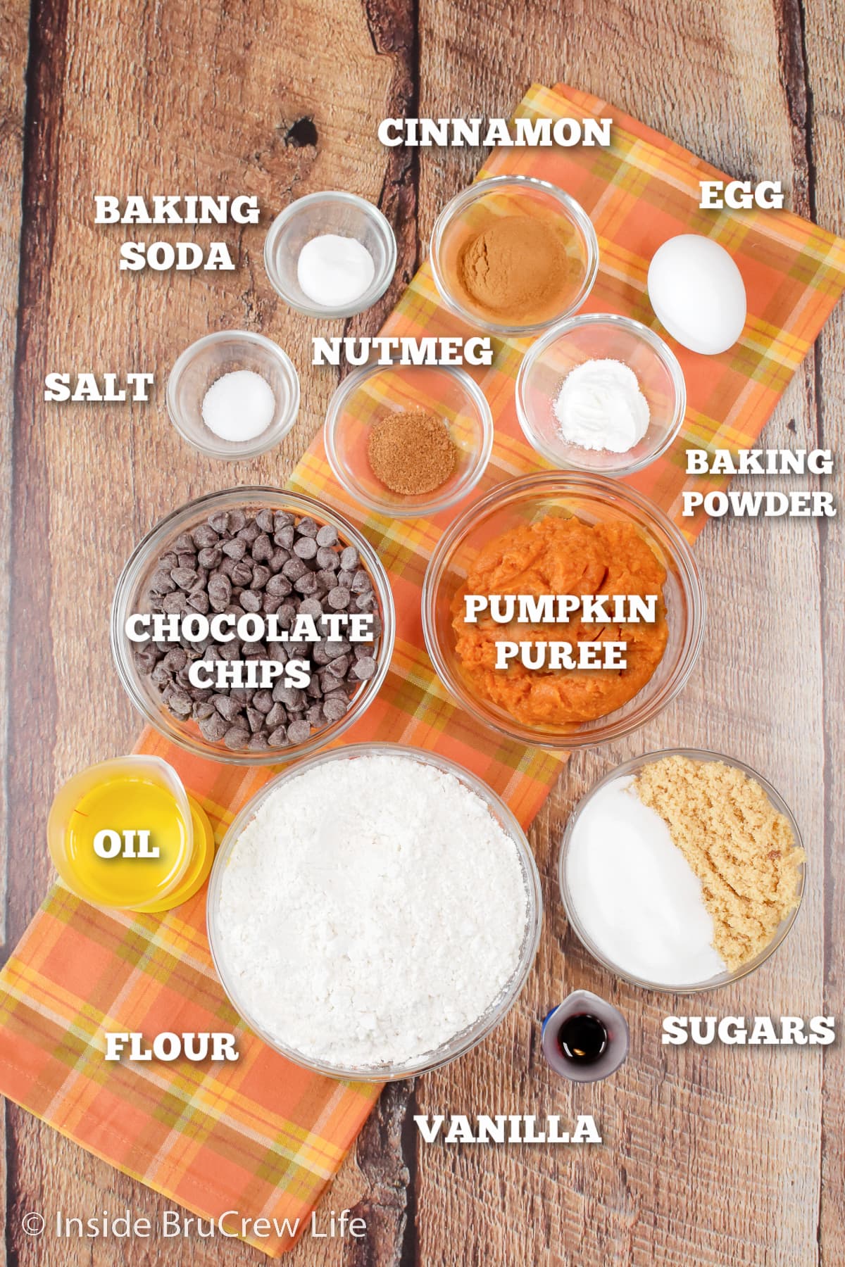 A brown board with bowls of ingredients needed for pumpkin cookies.