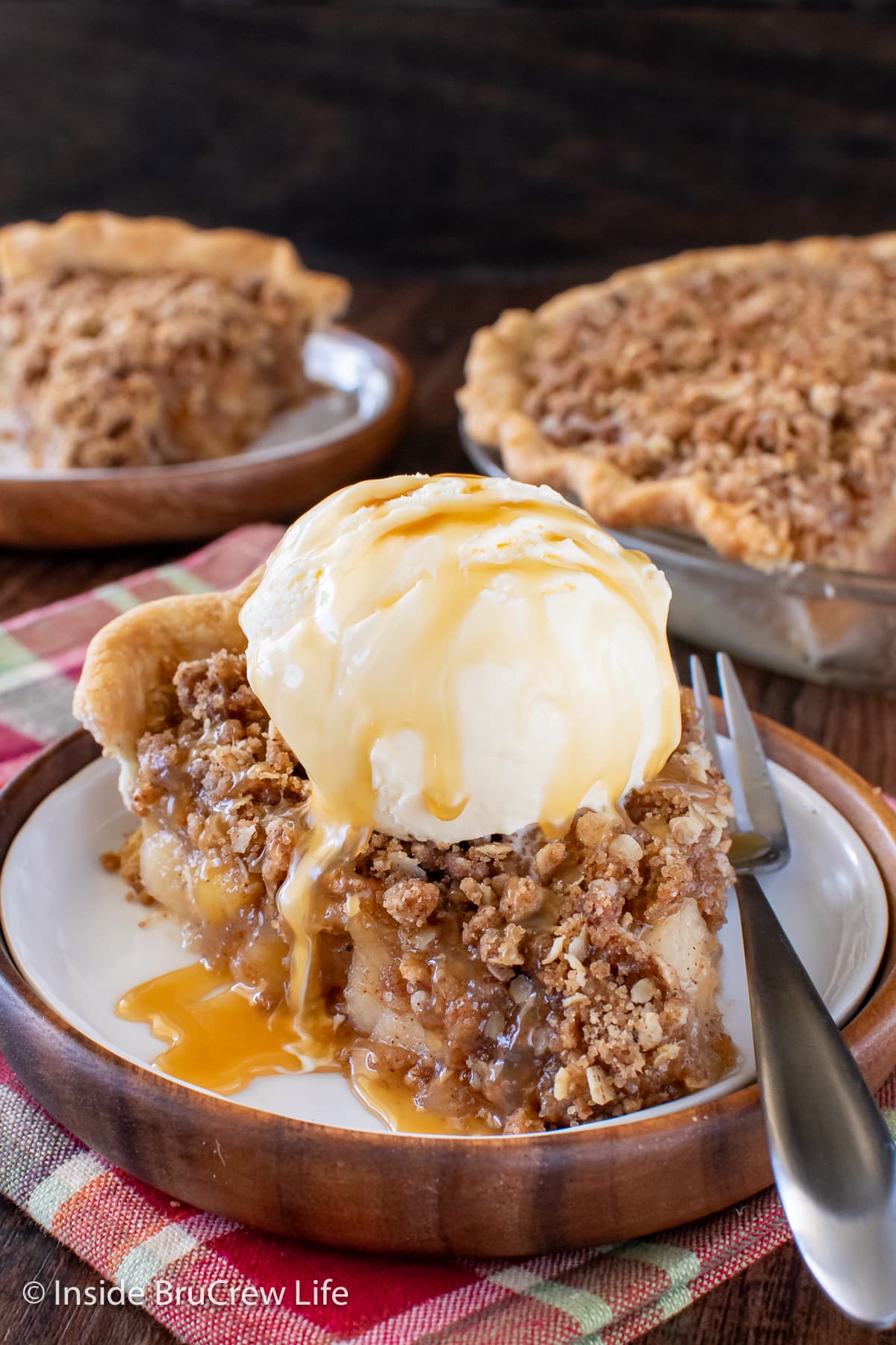 A slice of apple crumble pie topped with ice cream and caramel topping.