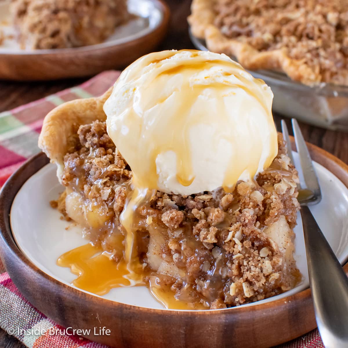 A slice of apple crumble pie topped with ice cream and caramel topping.