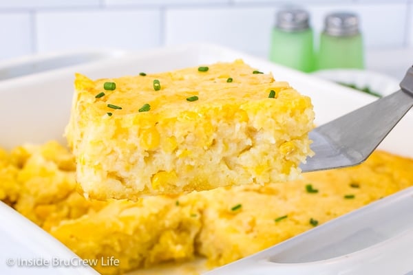 A square of corn casserole being lifted out of a white casserole dish.