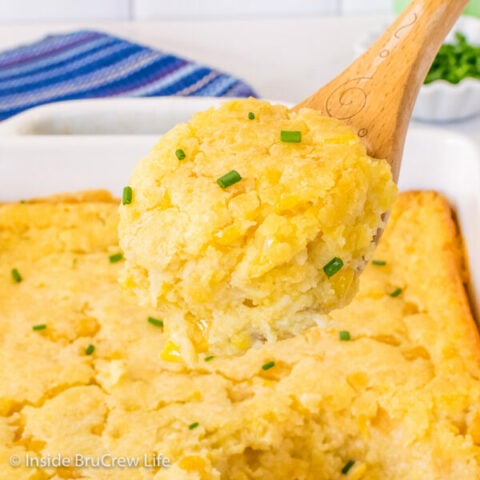 A wooden spoon lifting a scoop of Jiffy corn casserole out of a white casserole dish.