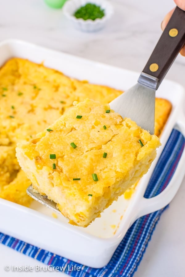 A spatula lifting a square of Jiffy corn casserole up and out of a white casserole dish.