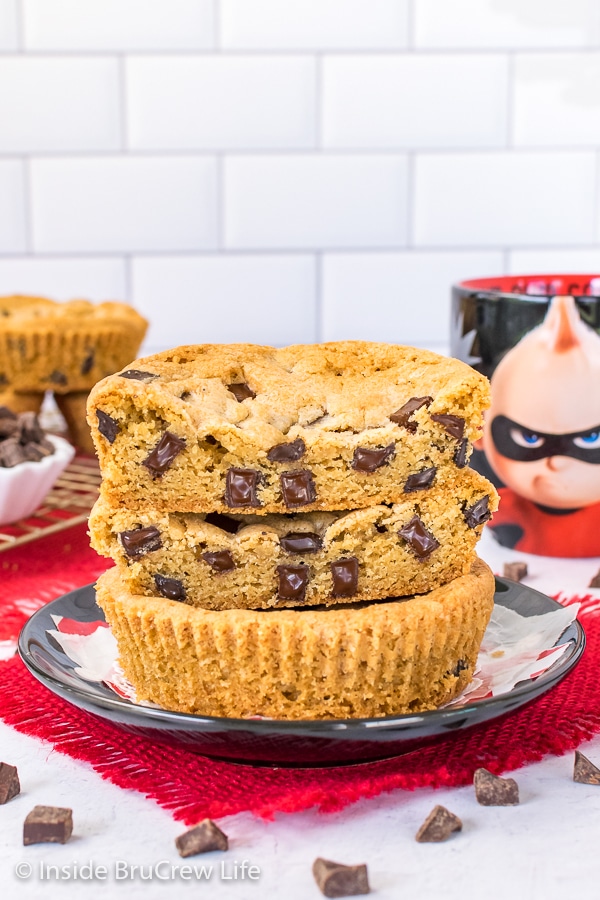 A giant cookie cut in half showing the melty chunks inside stacked on a black plate.