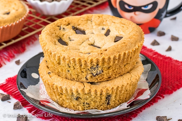 Two giant chocolate chip cookies stacked together on a black plate.