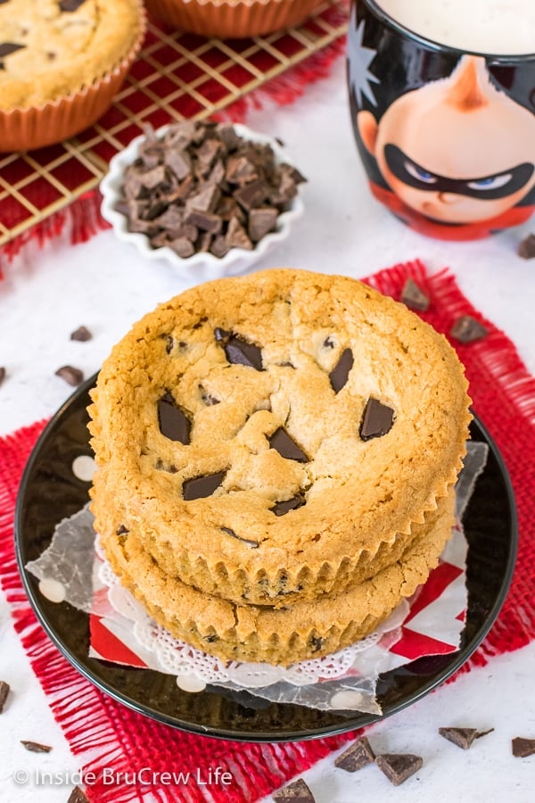 Two cookies stacked on a black plate with a bowl of chocolate chunks behind it.