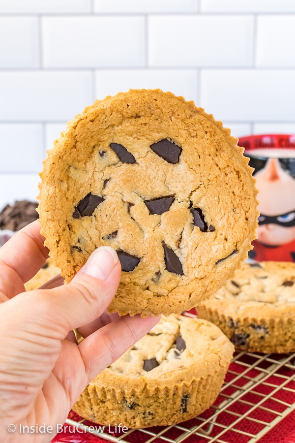 A giant chocolate chip cookie with chocolate chunks on top held up in front of a white background.