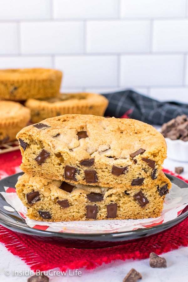 A chocolate chunk cookie cut in half and stacked on a black plate showing the melty chunks inside.