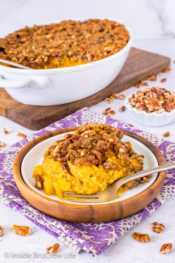 A white and brown plate on a purple towel with a scoop of sweet potato souffle on it