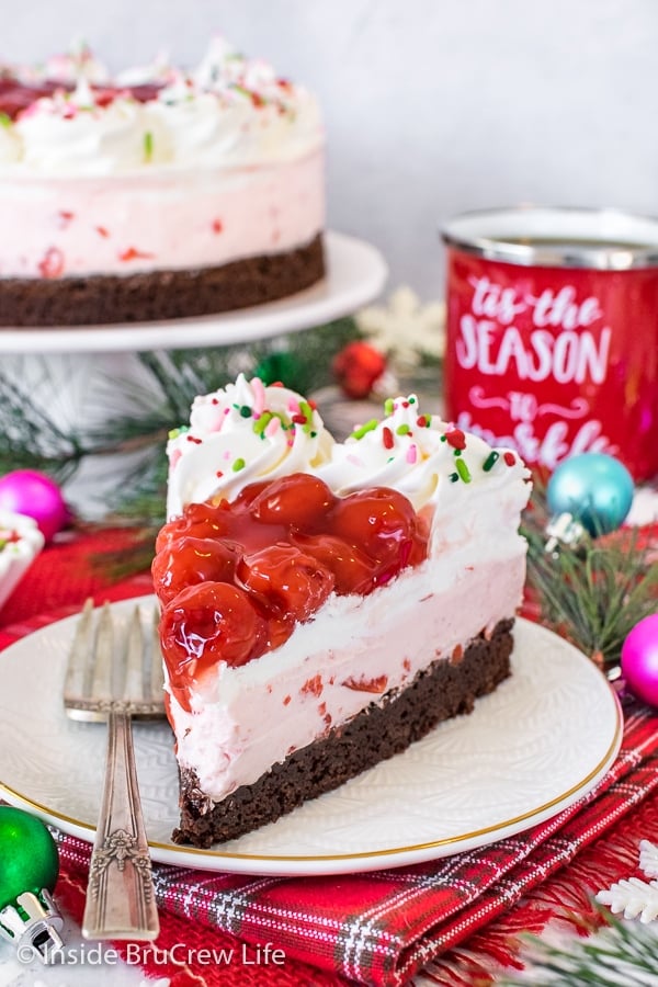 A white plate with a fork and slice of cherry mousse brownie cake on it and a cake plate with more cake behind it.