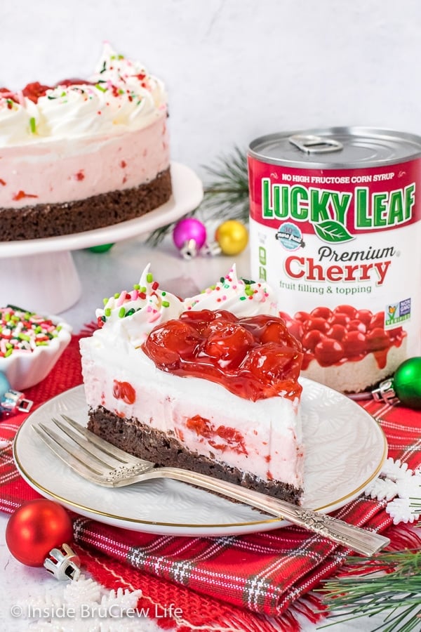 A white plate with a slice of cherry mousse brownie cake and fork on it and plate with more cake behind it.