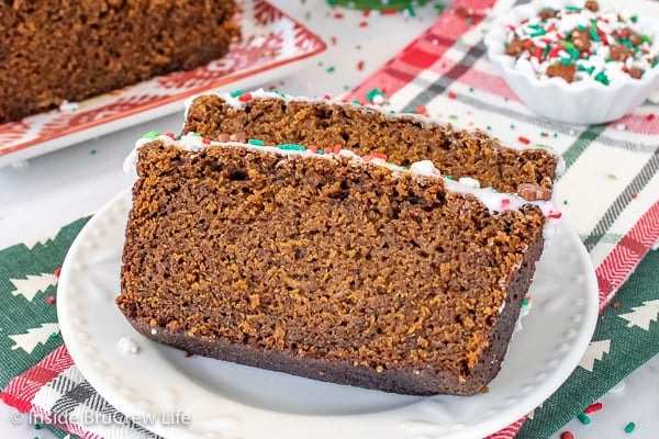 Two slices of frosted gingerbread banana bread on a white plate with a bowl of sprinkles behind it.