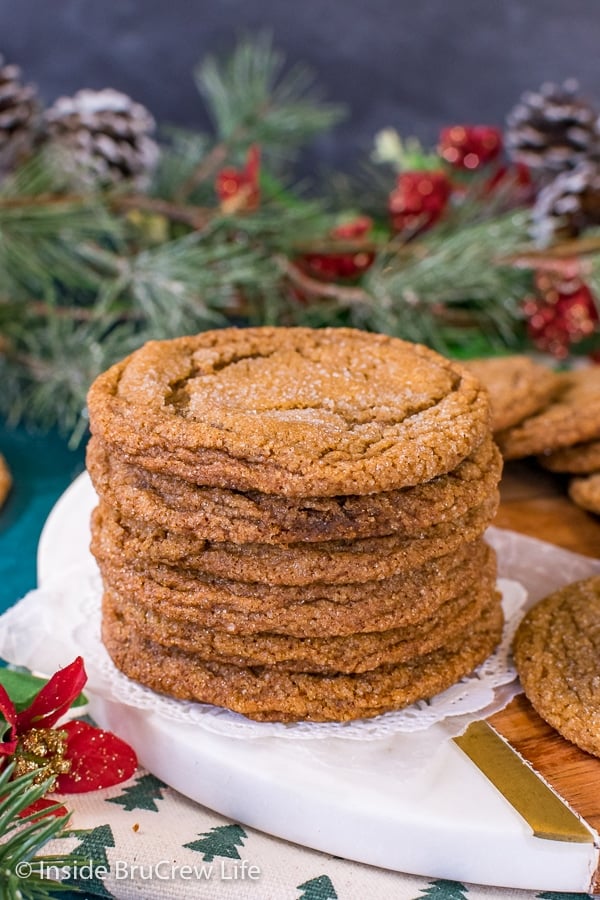 A stack of molasses crackle cookies on a white and brown tray with greenery behind it