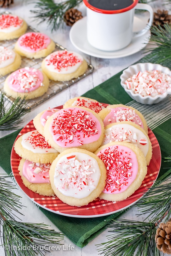 A red plate on a green towel with cookies topped with white and pink glaze and peppermint candies.