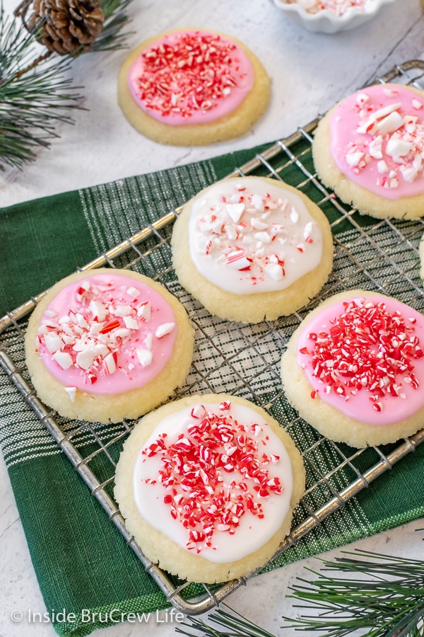 A wire rack on a green towel with cookies topped with pink and white glaze and peppermint candies on it