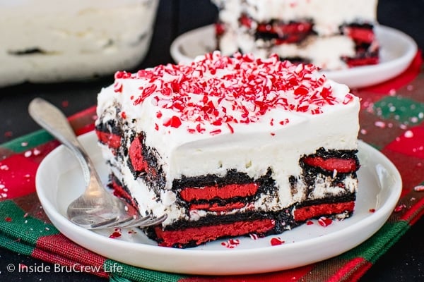 A red and green towel with square of peppermint oreo icebox cake topped with peppermint candies on a white plate