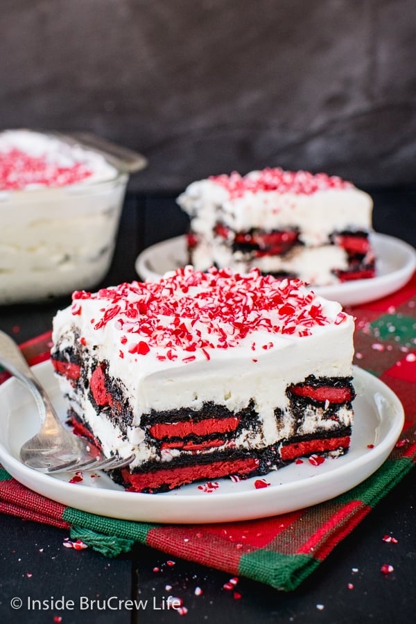 Two white plates on a holiday towel with squares of peppermint oreo icebox cake topped with crushed peppermint bits on top