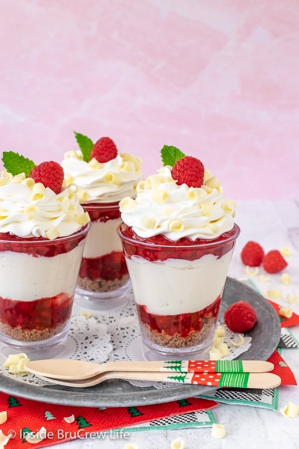 Raspberry White Chocolate Cheesecake Parfaits - layers of no bake cheesecake and raspberry pie filling with a cookie crust are an easy dessert to make. Great recipe for the holidays! Three clear cups filled with raspberry parfaits.