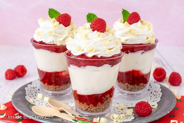 Three Raspberry White Chocolate Cheesecake Parfaits on a metal tray with a pink background
