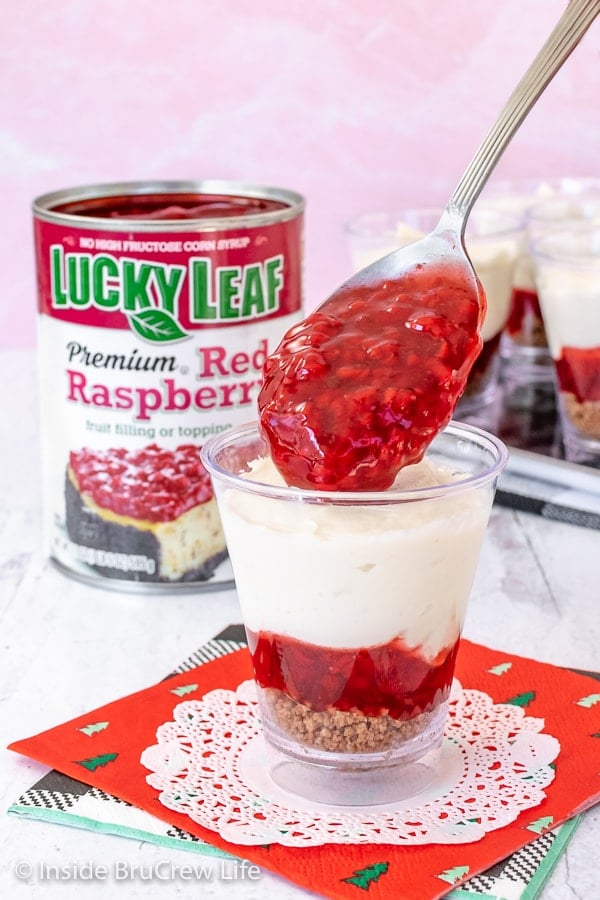 A clear cup with white chocolate cheesecake and spoonful of raspberry pie filling going into the top
