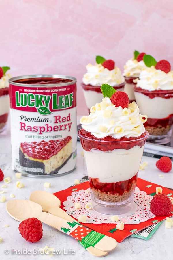 Cups of raspberry white chocolate cheesecake parfaits and a can of pie filling on a white board