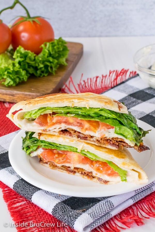 A BLT tortilla wrap hack cut in half and stacked on a white plate showing the inside fillings